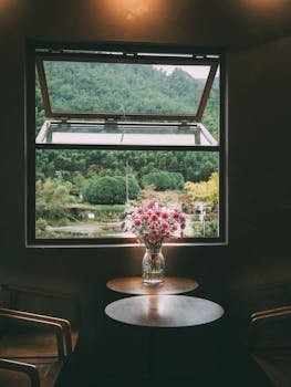 A cozy room with a vase of flowers by a window offering a scenic view of lush greenery.